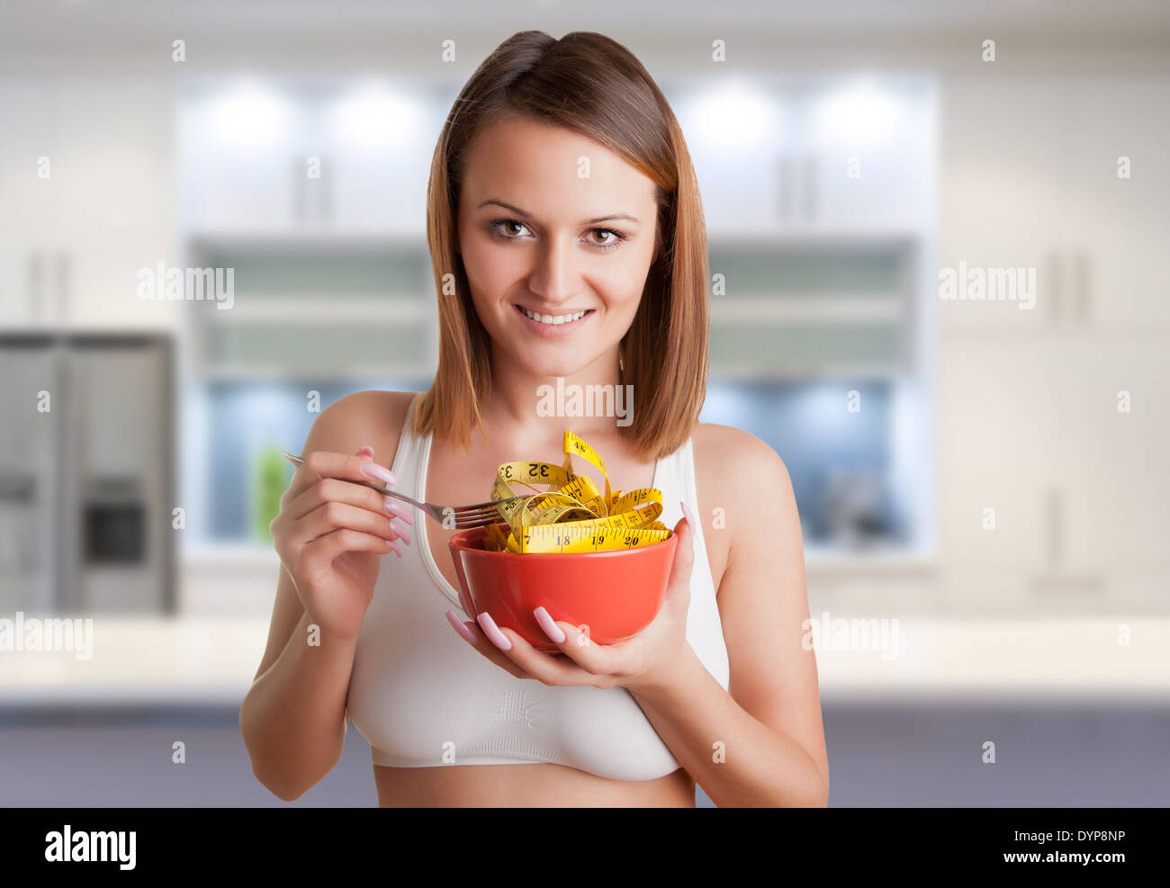 Concept image of a woman on a diet, eating a measuring tape, in a kitchen Stock Photo