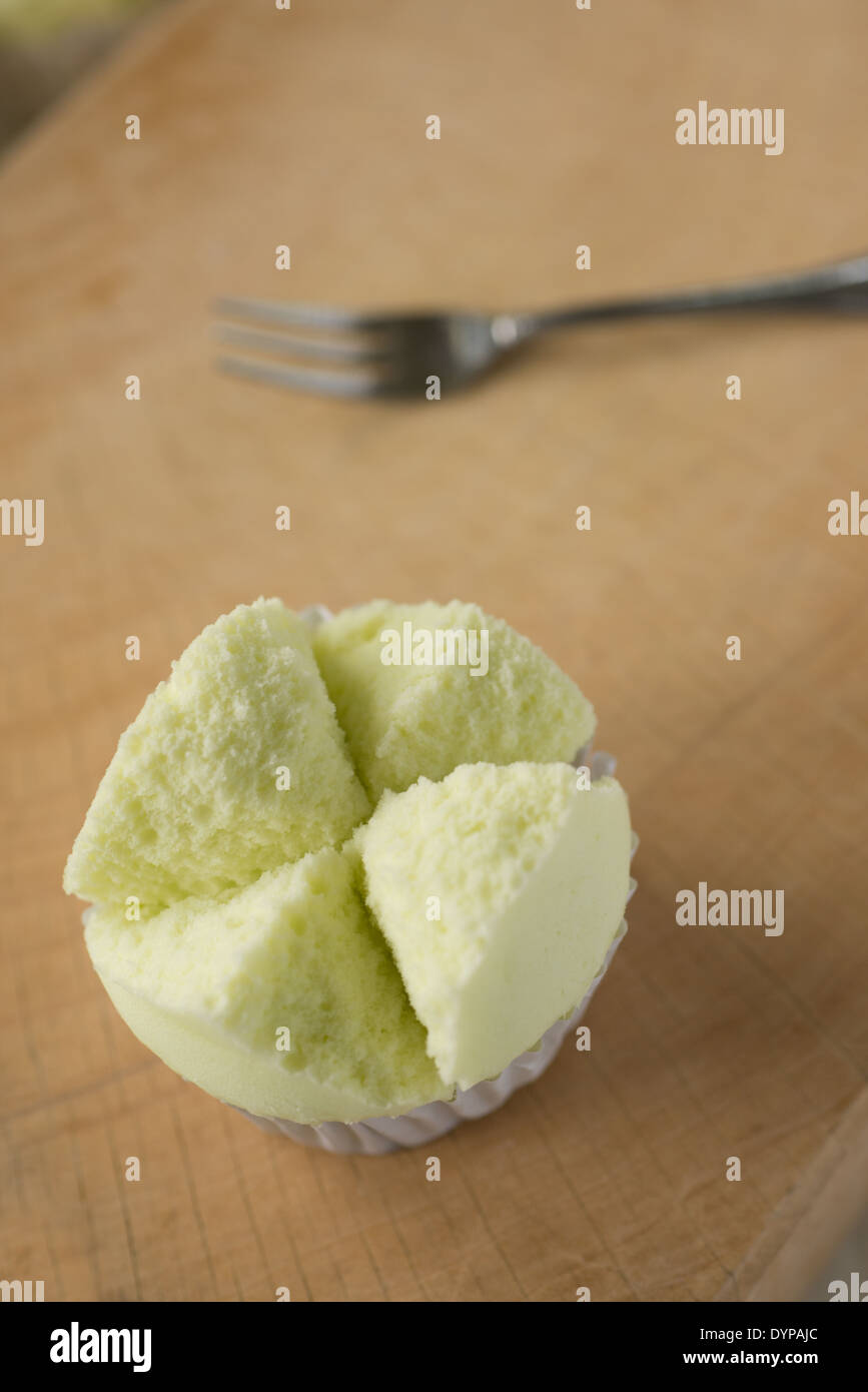 A top view shot of a beautiful light green Thai cup cake on a wooden block, a small dessert fork in the background. Stock Photo