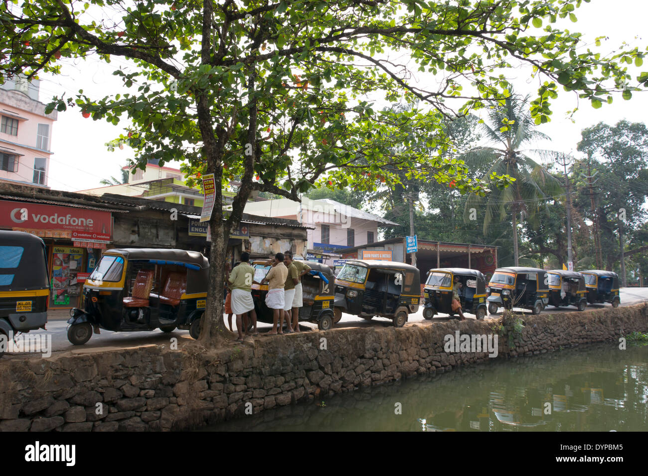 Auto Rickshaws and their drivers parked by a waterway in the backwaters of Kerala in India Stock Photo