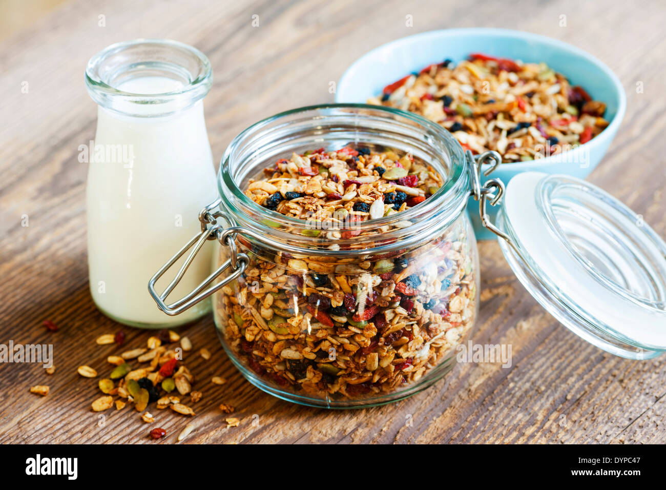 Homemade granola in open glass jar and milk or yogurt on rustic wooden