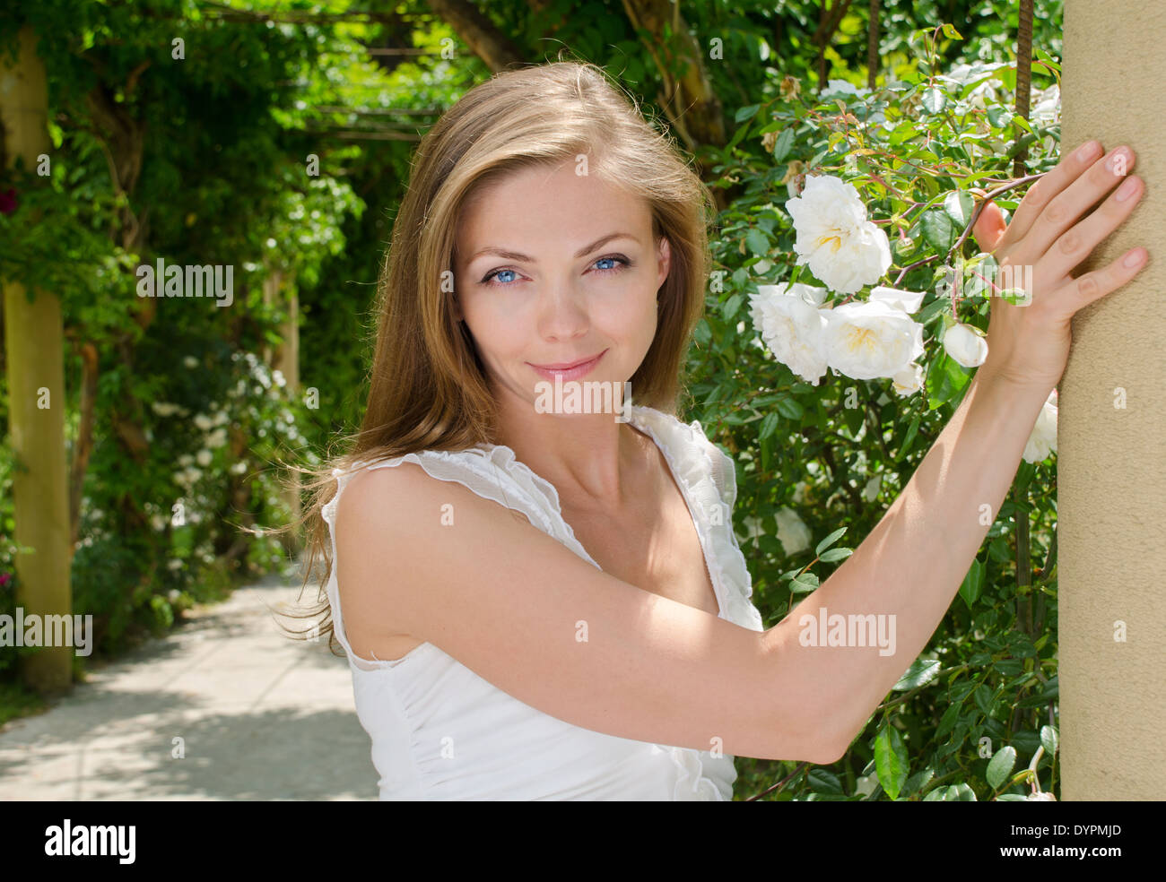happy woman with blond hair and blue eyes in the park on a background of flowers Stock Photo