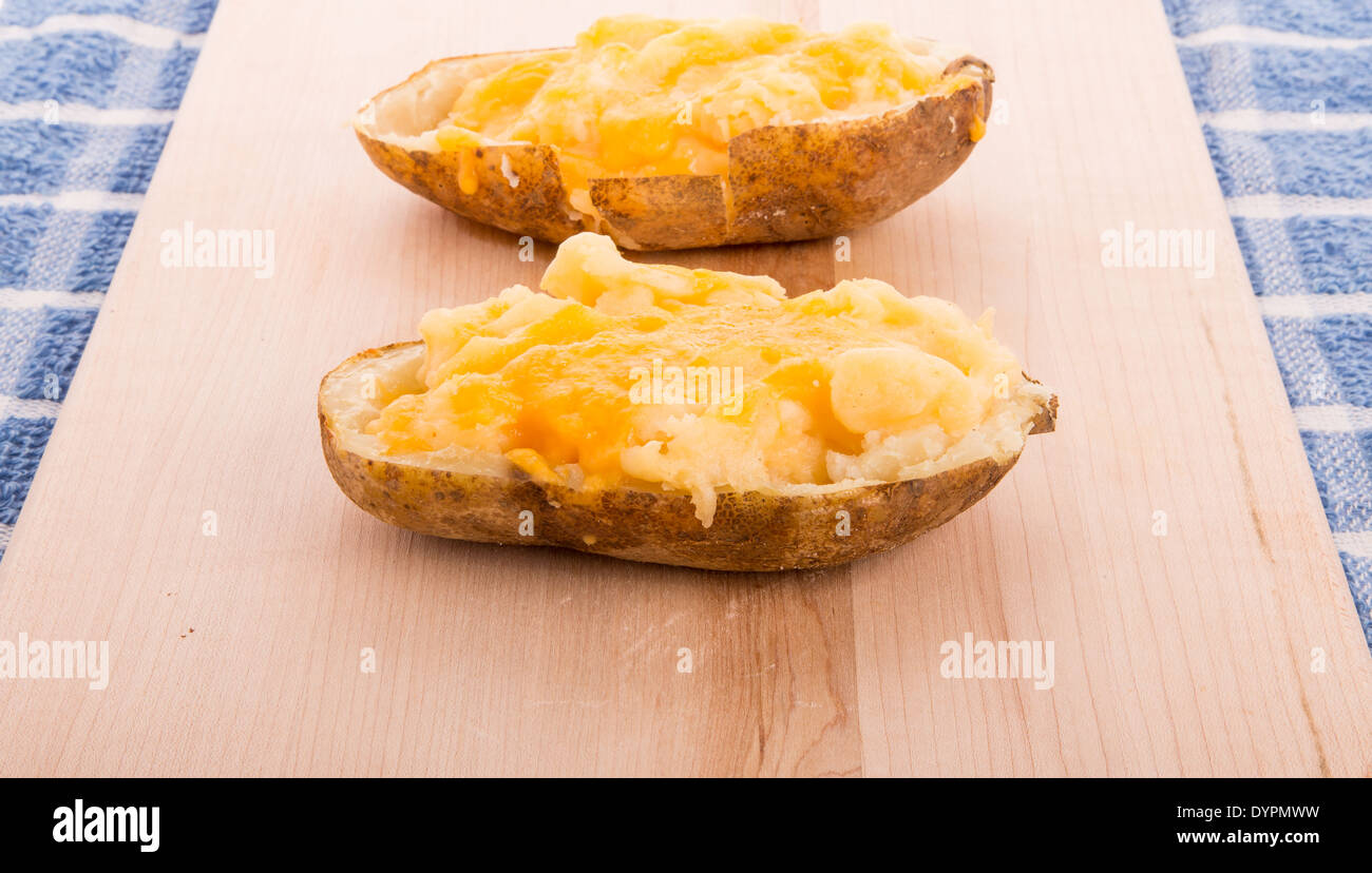 Two halves of a baked potato topped with melted cheese on a wood Stock