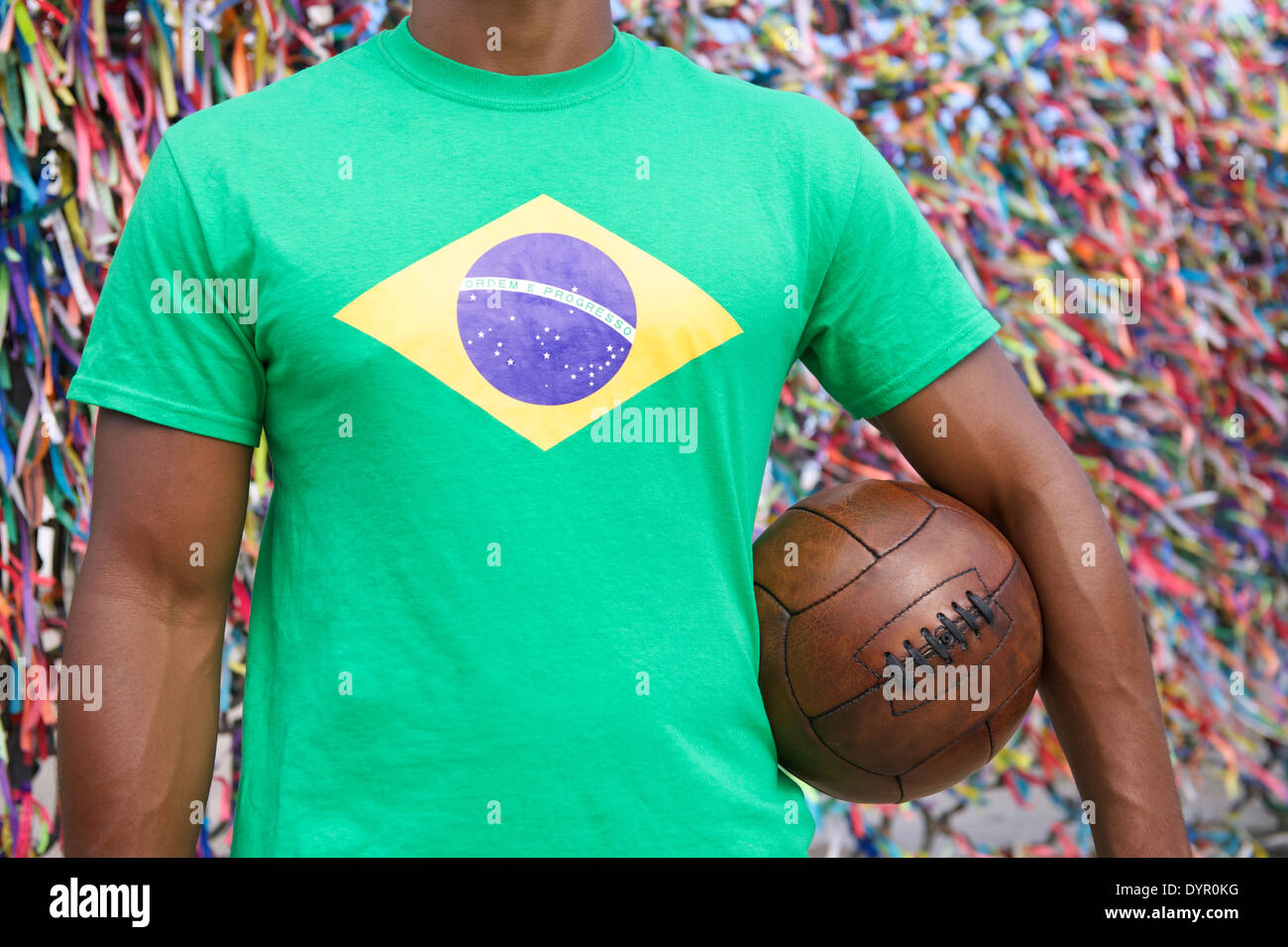 Brazilian soccer player standing with vintage brown football in front of wall of colorful lembranca wish ribbons Salvador Bahia Stock Photo