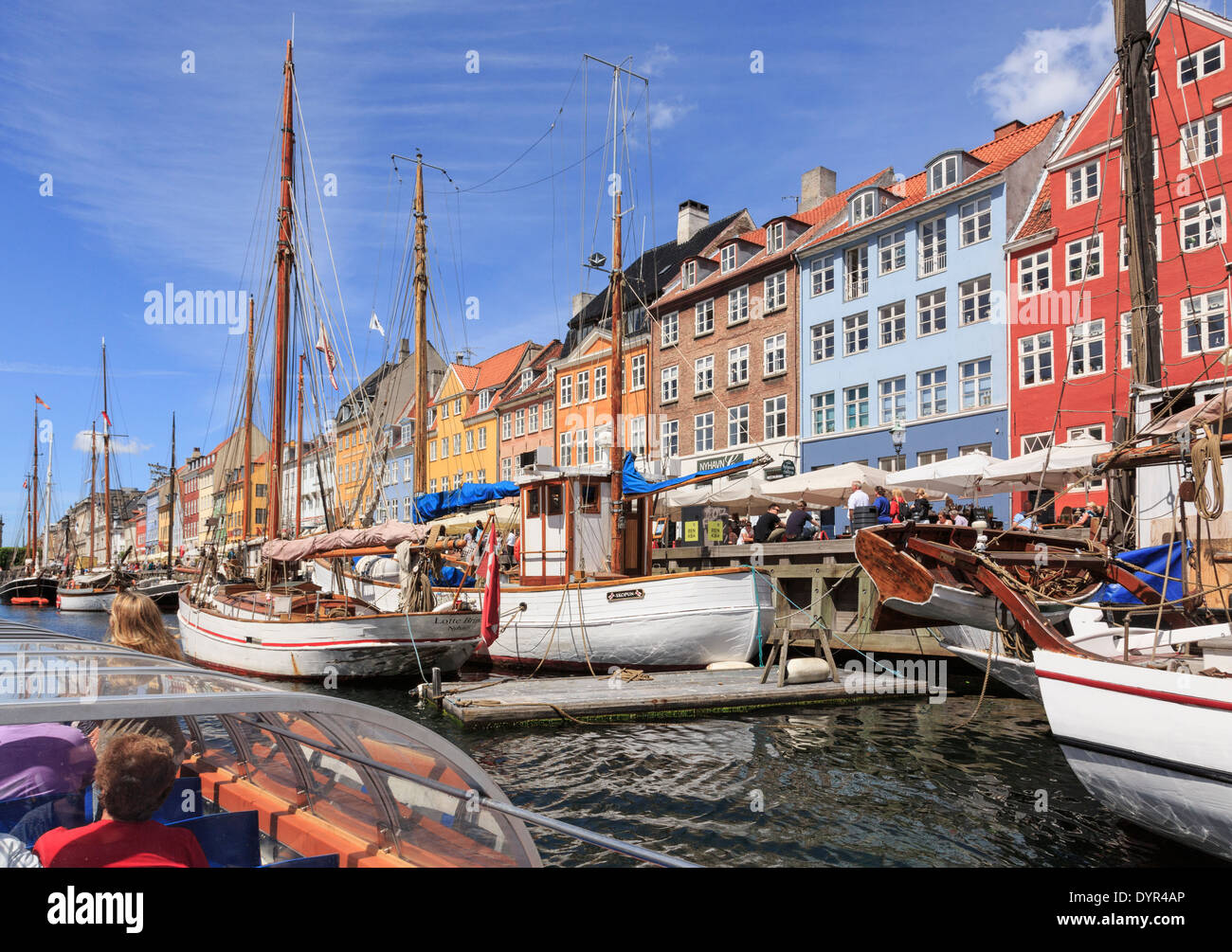 Tourists on Copenhagen canal tour boat with old wooden boats moored in front of colourful buildings on Nyhavn, Copenhagen, Zealand, Denmark Stock Photo