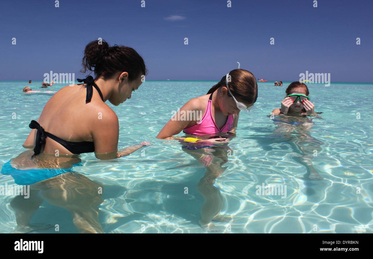 Three young girls looking for shells in a shallow turquoise water of the Caribbean Sea in Varadero, Cuba Stock Photo