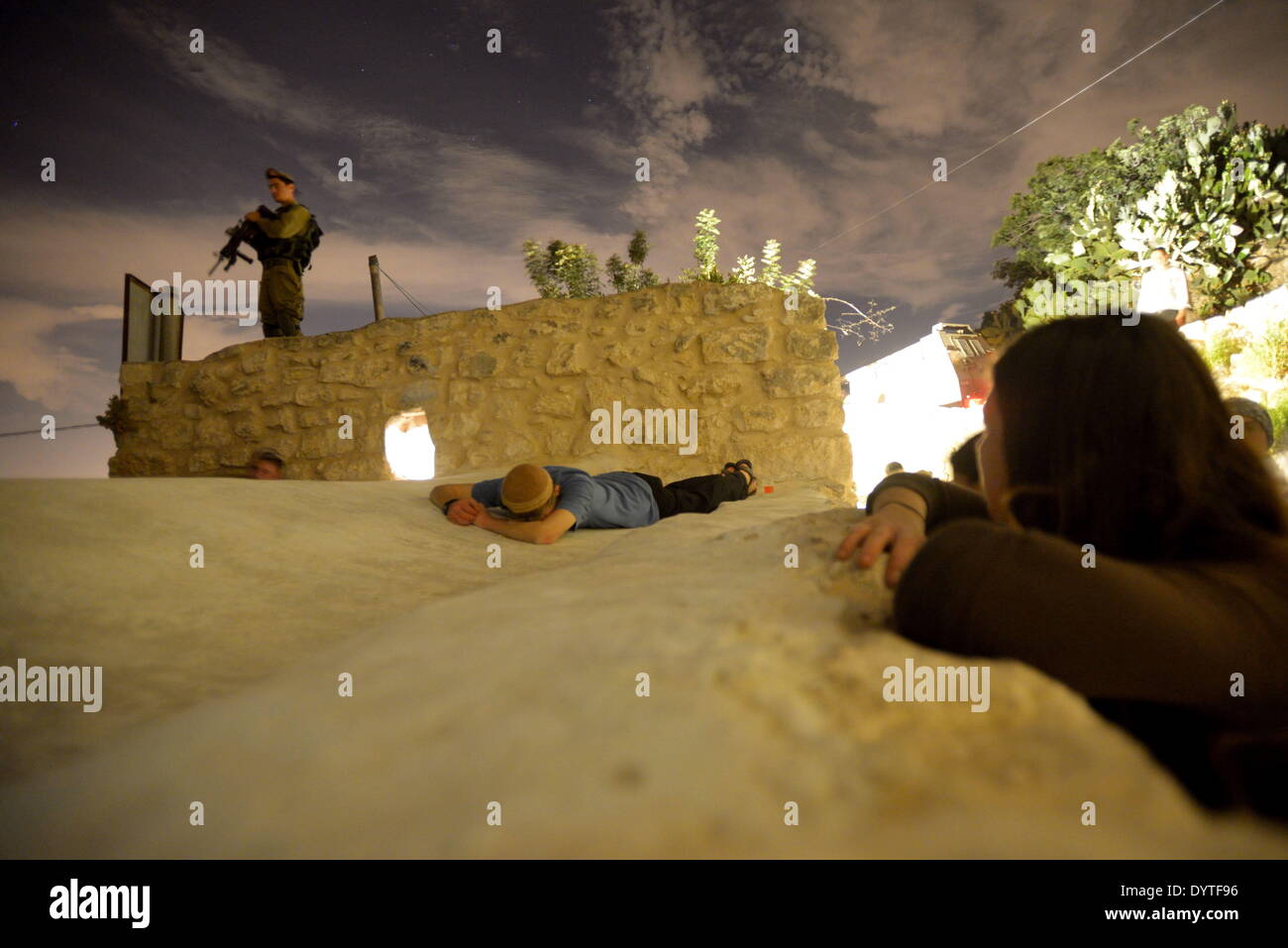 April 25, 2014 - Kifl Hareth, West Bank - KIFL HARETH, WEST BANK - APRIL 24: An Israeli soldier stands guard as an Ultra-Orthodox Jews lays on the tomb of Nun, father of Biblical Israelite spy and leader Jehoshua Bin Nun (Joshua), on April 24, 2014 in the northern West Bank Palestinian village of Kifl Hareth. Thousands of religious Jews entered the village after midnight under heavy Israeli army guard to pray at the tombs of Bin Nun and Calev Ben Yefuneh on the traditional anniversary of Bin Nun's death. They were the two Jewish spies who reported to Moses that the Holy Land, which Jews believ Stock Photo