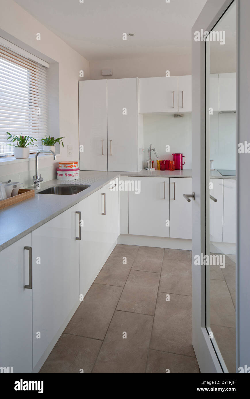 Open door to small white modest modern kitchen with tiled floor. Stock Photo