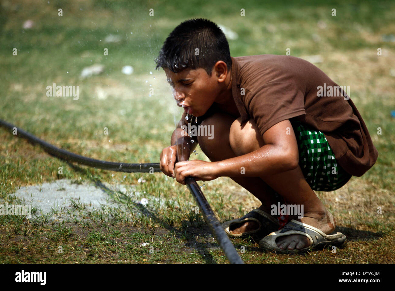 A boy drinking water from water pipe while playing on field.People in