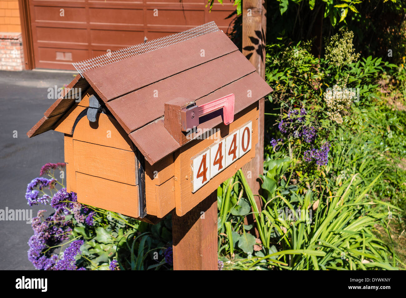 A house shaped wooden mailbox with bird deterrent on top and address on
