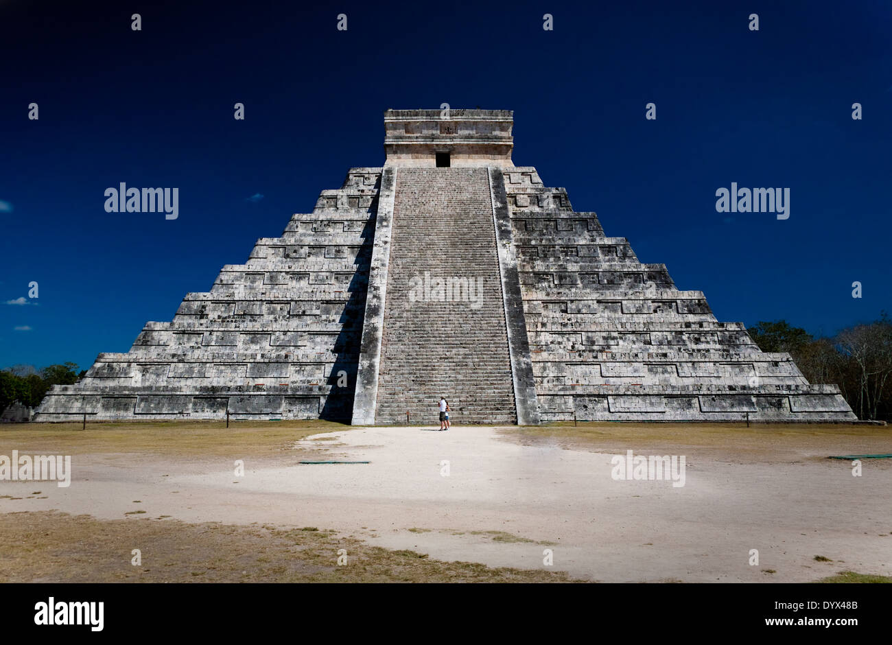 Ziggurat (pyramid) at Chichen Itza with two people staring at it in front of the stairway. Dark blue sky Stock Photo