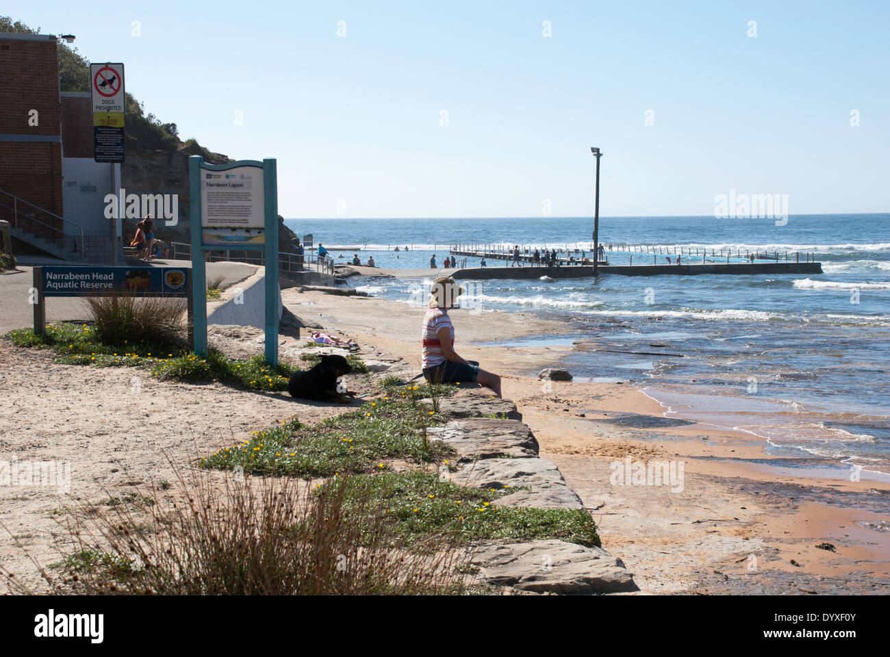 A woman sitting on a stone wall at North Narrabeen beach and lagoon, Sydney. Stock Photo
