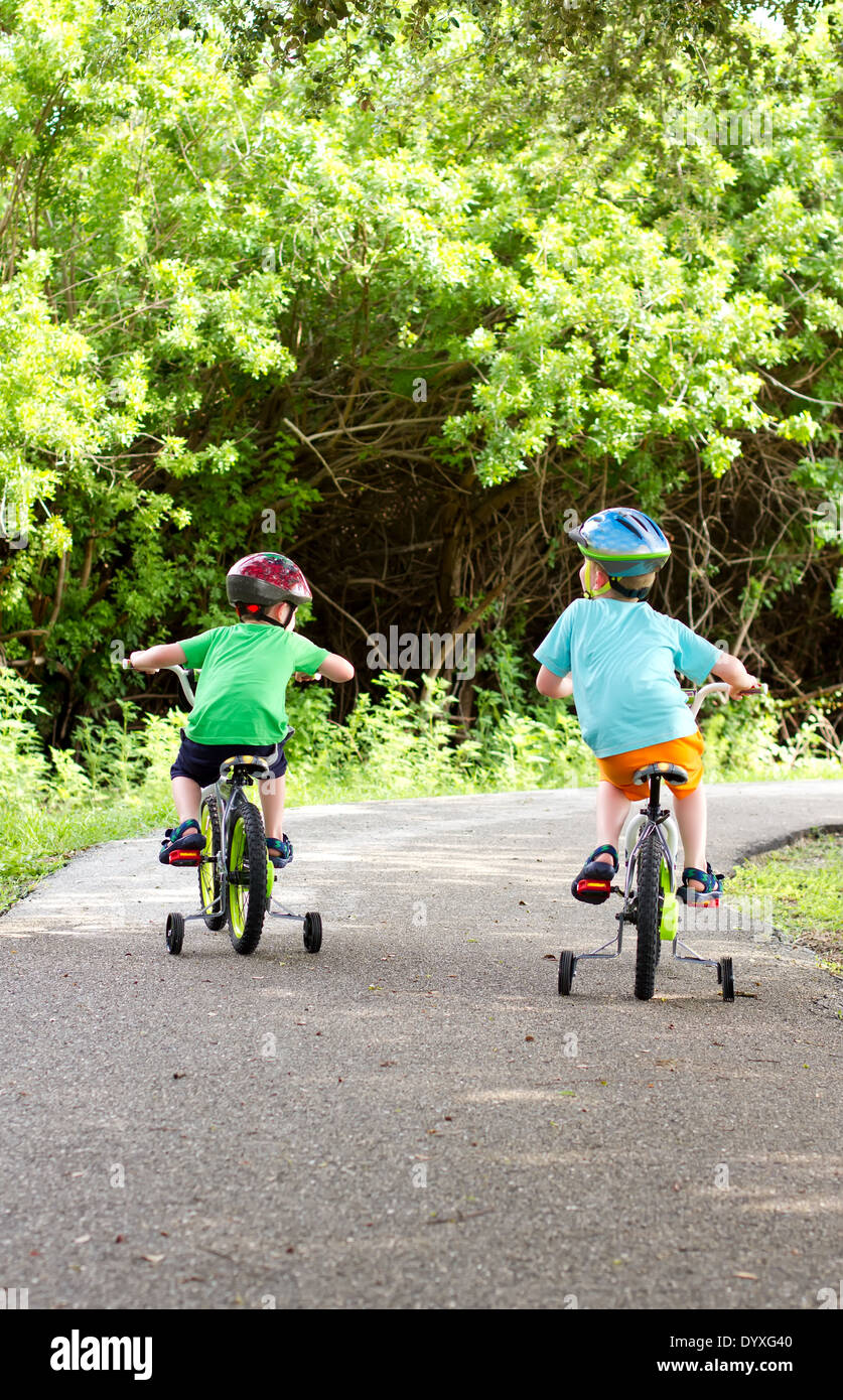 two little boys riding their bikes along a shaded park trail Stock Photo