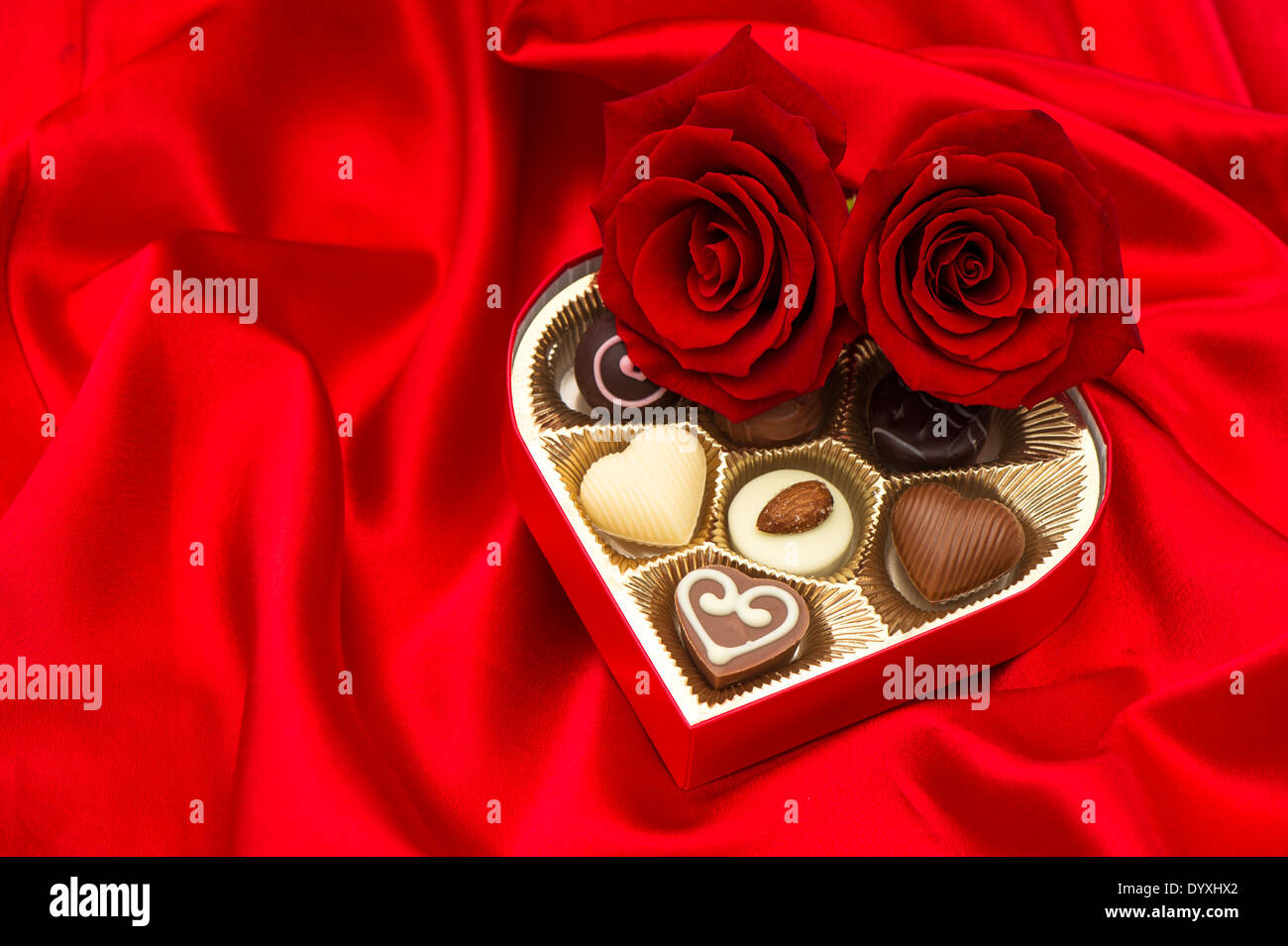 red roses and assorted chocolate pralines in golden heart shaped gift box on satin background Stock Photo