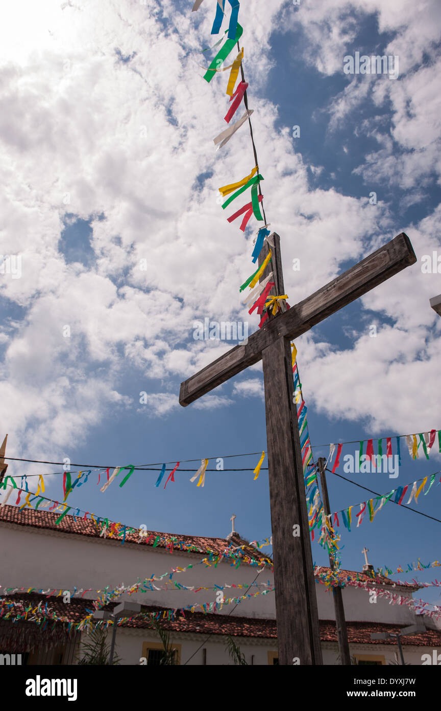 Itaparica Island, Bahia State, Brazil. Itaparica town. Wooden cross with colourful bunting outside a colonial church. Blue sky and white clouds. Stock Photo