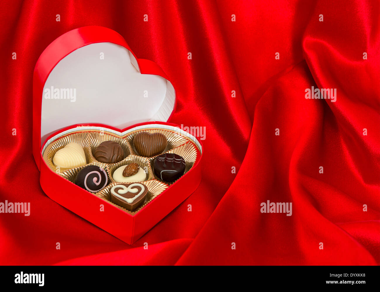 chocolate pralines in golden heart shape box over red silk background. Valentine's Day gift. space for your text Stock Photo