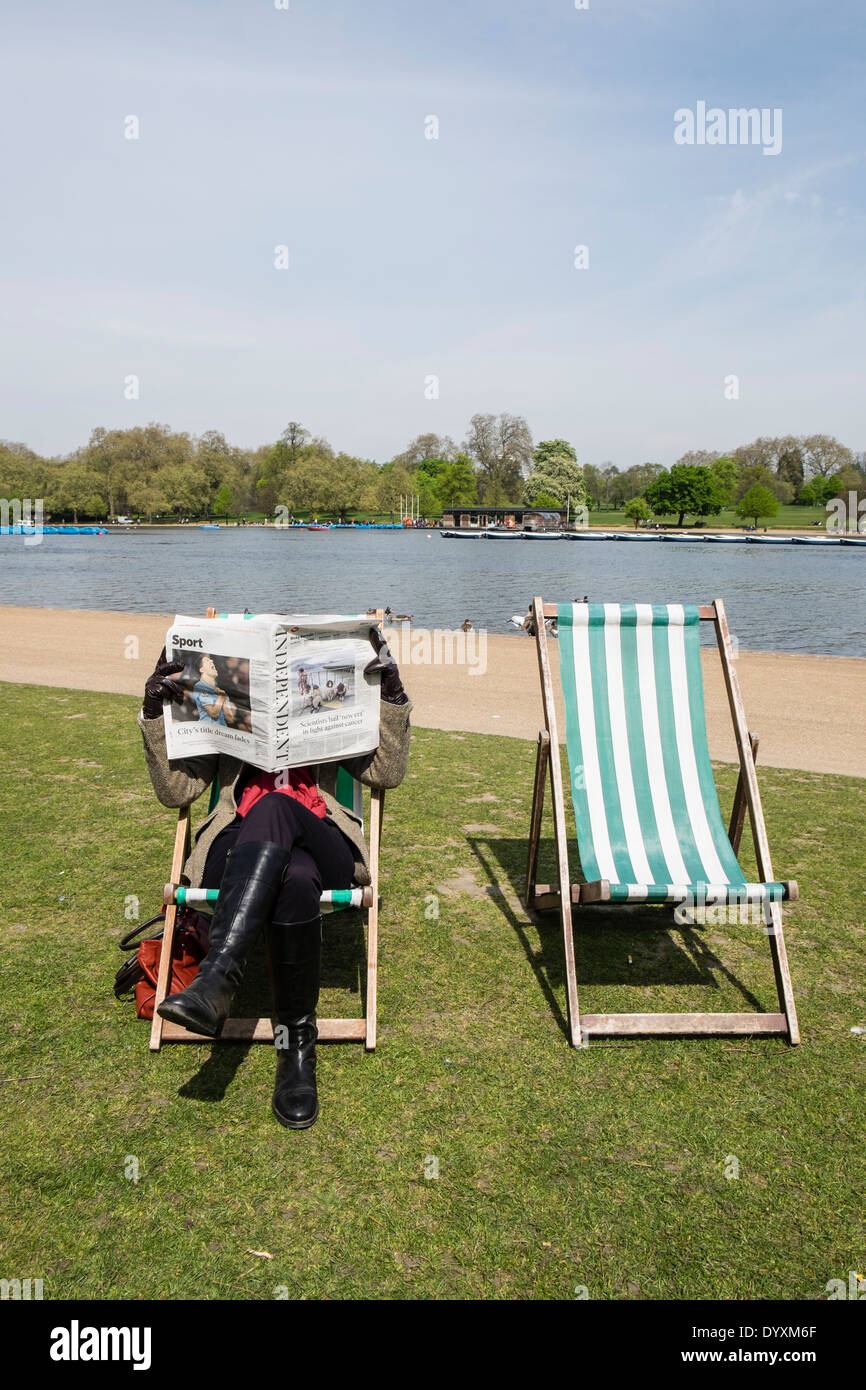 Woman reading a newspaper sitting on a deckchair in Hyde Park in London United Kingdom Stock Photo