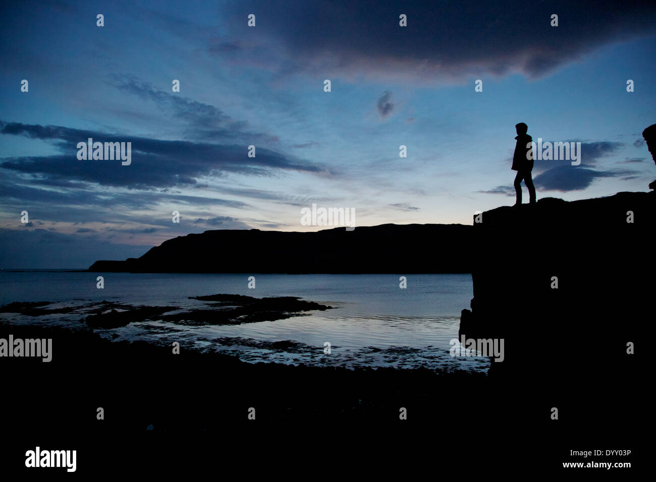 Boy stands on boulder silhouetted,evening light,Calgary bay at dusk,  sle of Mull, Argyle,Hebrides,Scottish Highlands,Scotland Stock Photo