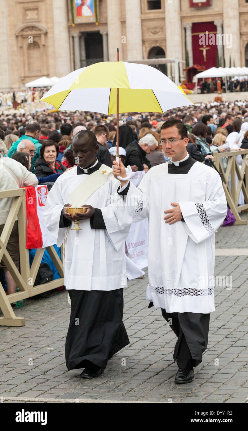 An African and a Chinese priest together going to give holy communion to the pilgrims gathered in Saint Peter's Square. Stock Photo