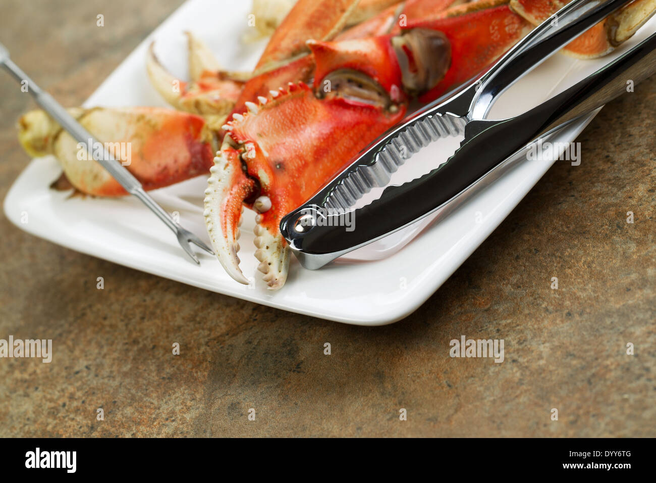 Closeup horizontal photo of freshly cooked Dungeness crab legs on white plate with stainless crab crackers and stone counter top Stock Photo