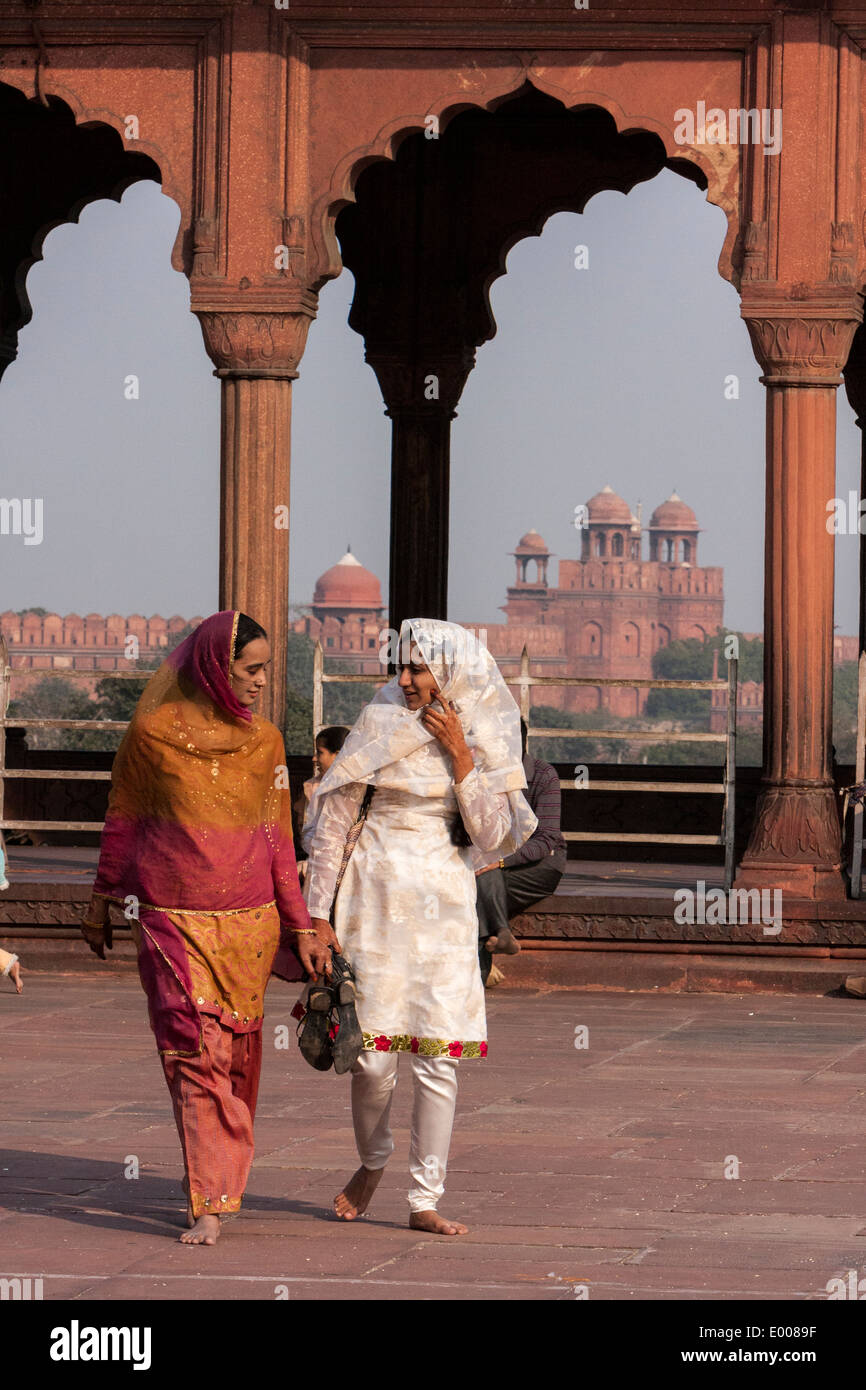 New Delhi, India. Muslim Indian Women Walking in the Courtyard of the Jama Masjid (Friday Mosque). Red Fort in the Background. Stock Photo