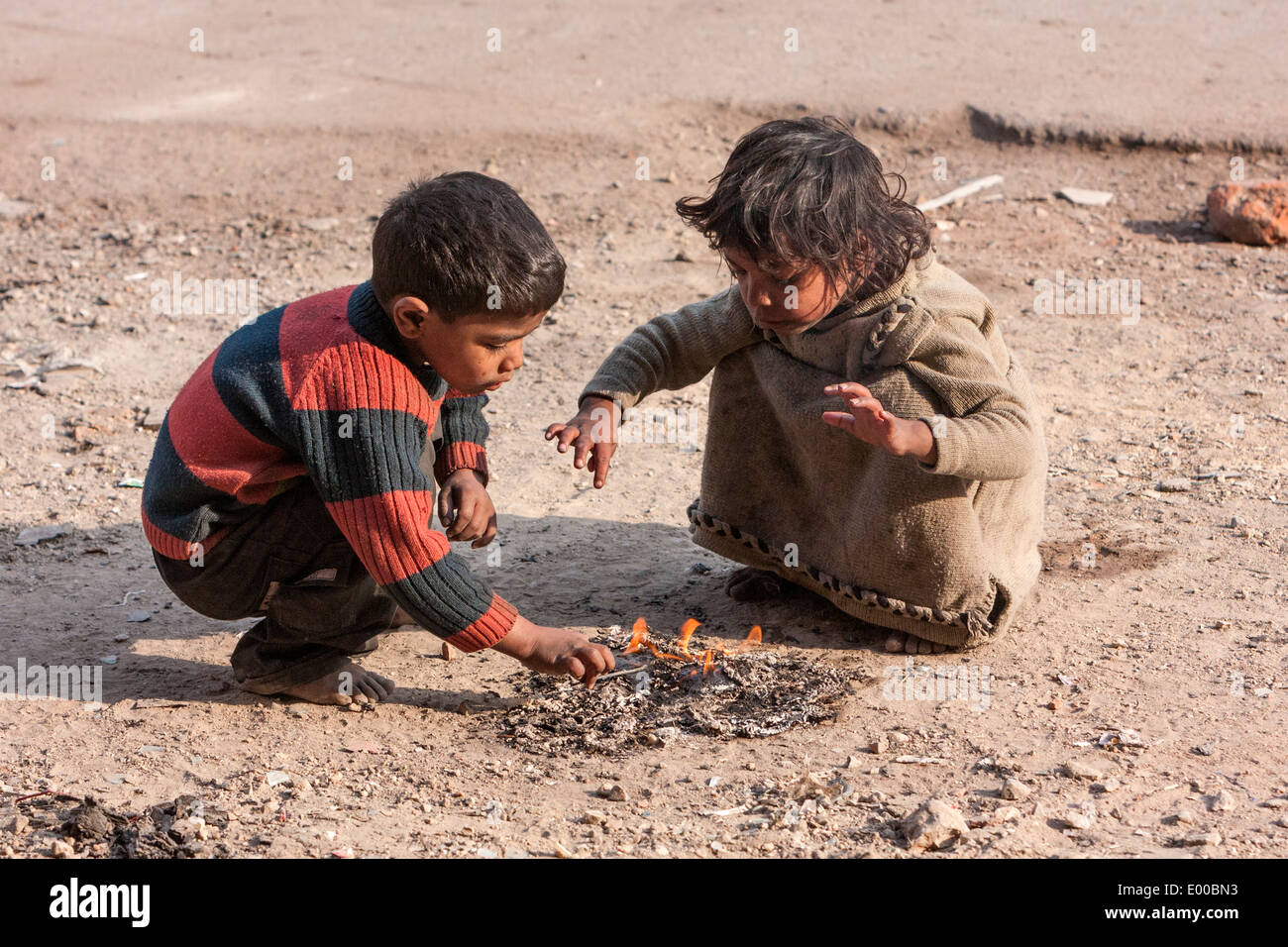 New Delhi, India. Little Boy and Girl Warming themselves by a Fire alongside the Street in Downtown Delhi. Stock Photo