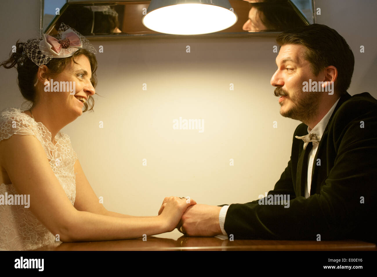 Happy bride and groom hold hands over a table in a dining both at a vintage wedding Stock Photo