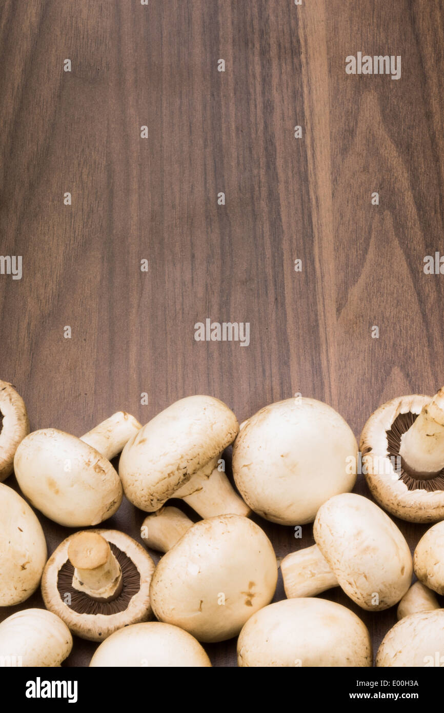 A bunch of button mushrooms/champignons bunched up at the bottom of the image on a brown background. Stock Photo