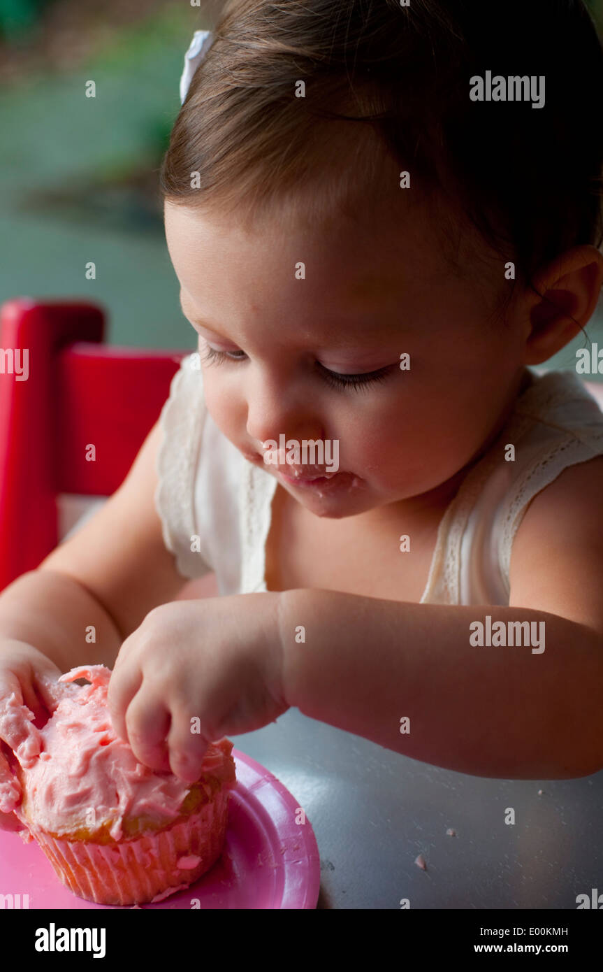 A little girl eating the frosting from a pink cupcake. Stock Photo