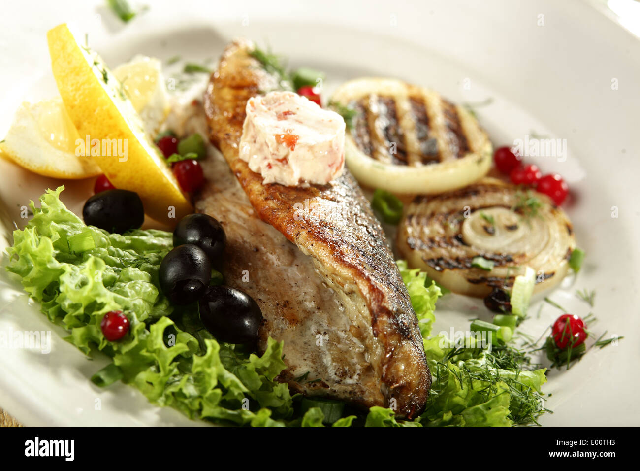 hot fish in white dish with olives and lemon Stock Photo - Alamy