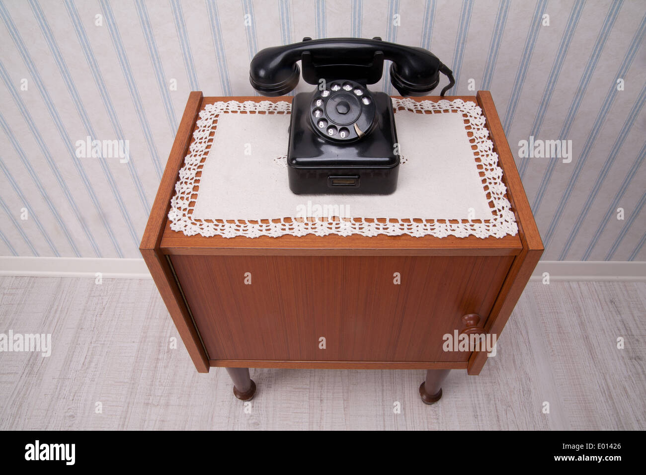 Black rotary dial telephone on a piece of furniture with old fashioned striped wallpaper Stock Photo
