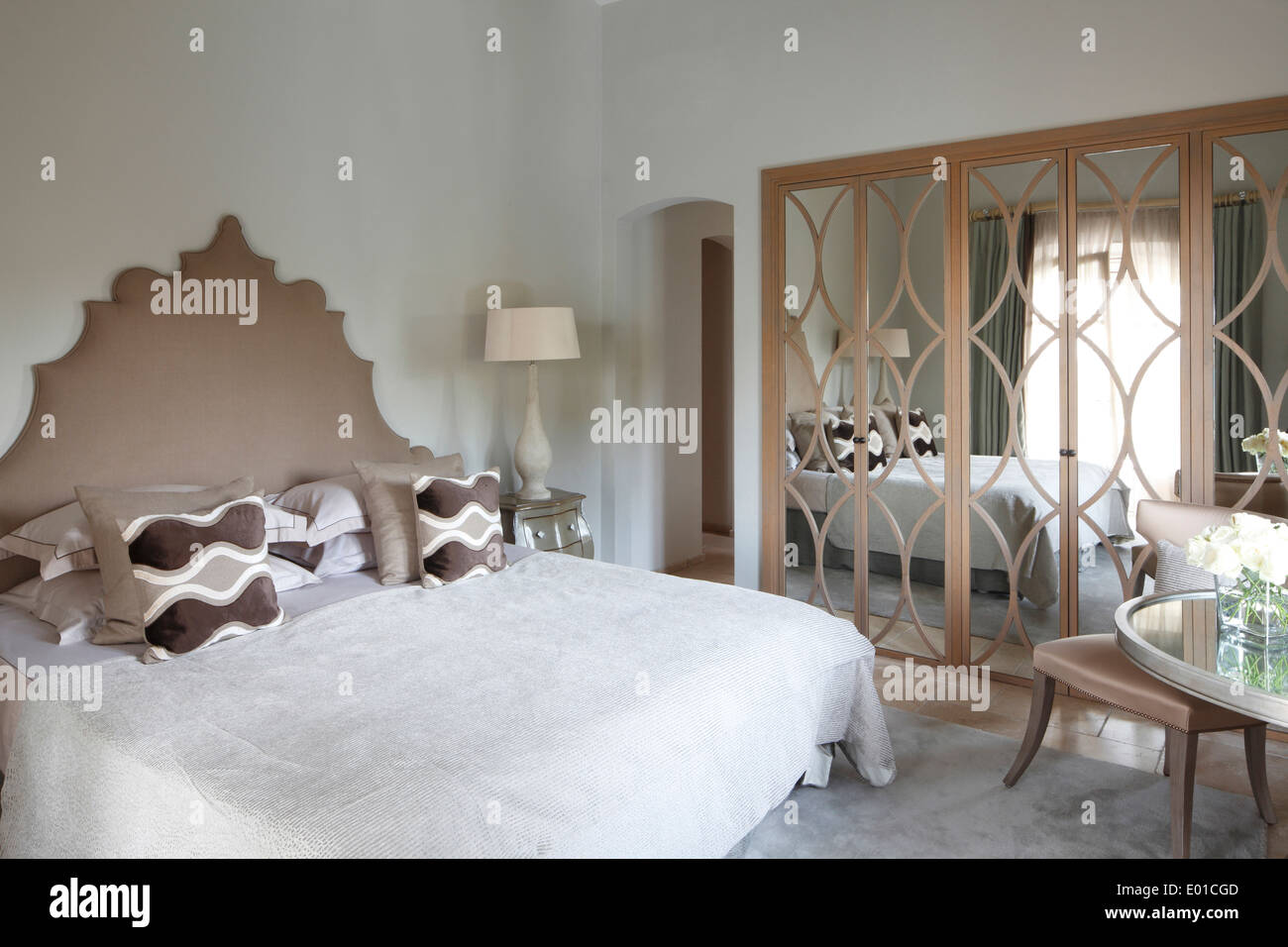 Guest bedroom with elaborate headboard and mirror panelled wardrobes