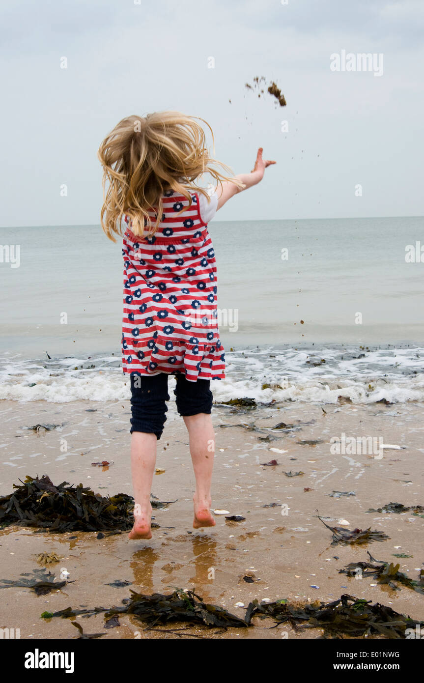 young girl jumping up and throwing sand into the sea Stock Photo