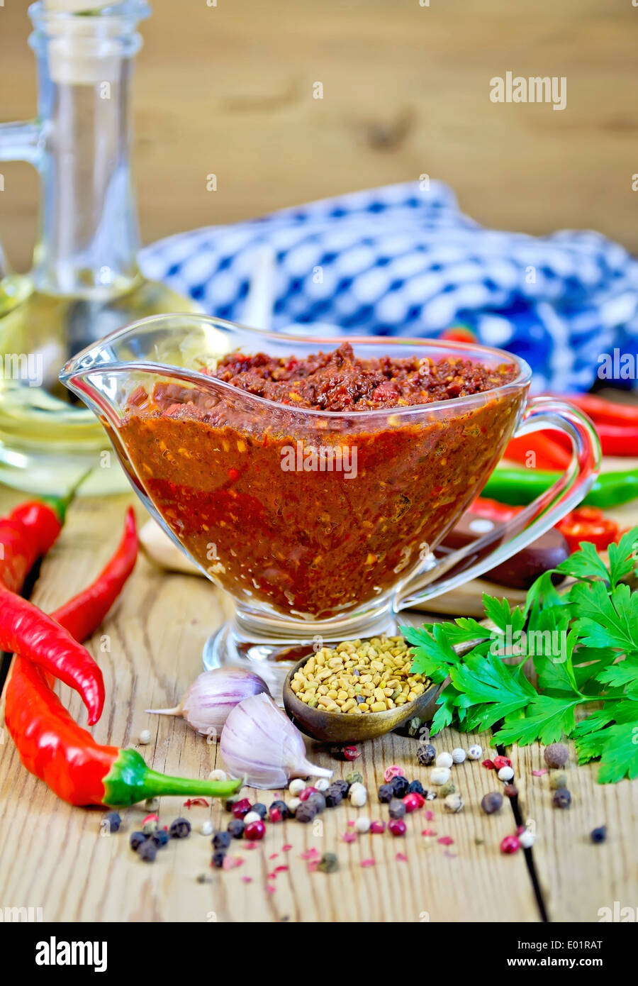 Tabasco adjika in a glass gravy boat, hot pepper, garlic, parsley, fenugreek, napkin, oil in a carafe on a wooden board Stock Photo