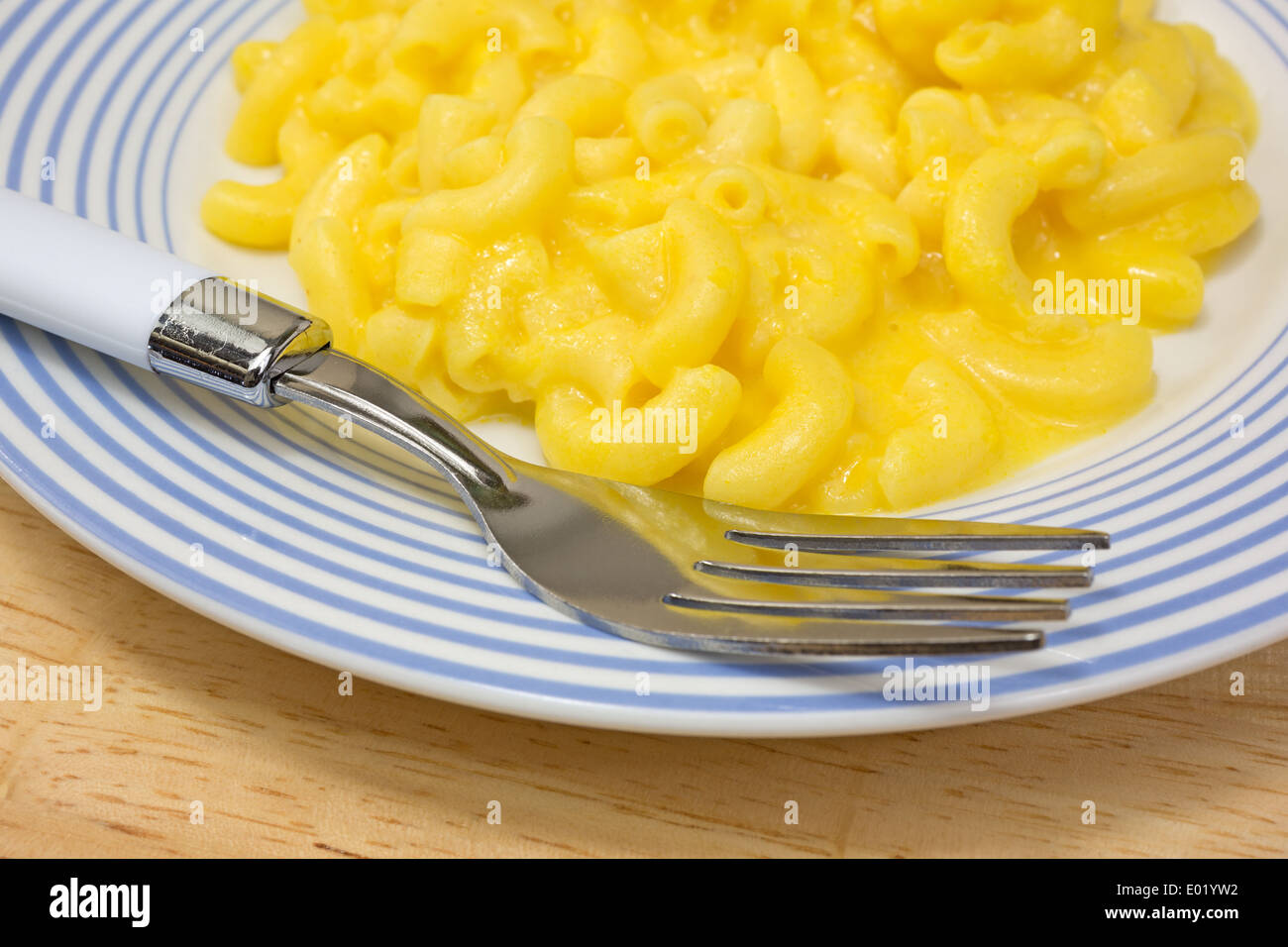 Close view of macaroni and cheese on a blue striped plate with fork on a dining table. Stock Photo