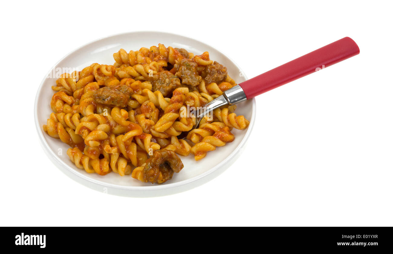 A serving of spiral pasta in a tomato sauce with chunks of Italian sausage on a plate with a red handled fork. Stock Photo