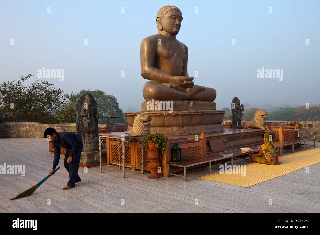 A man sweeps whilst a woman prays at dawn at the statue of Lord Mahavira at the Ahinsa Sthal Jain temple, Delhi, India Stock Photo