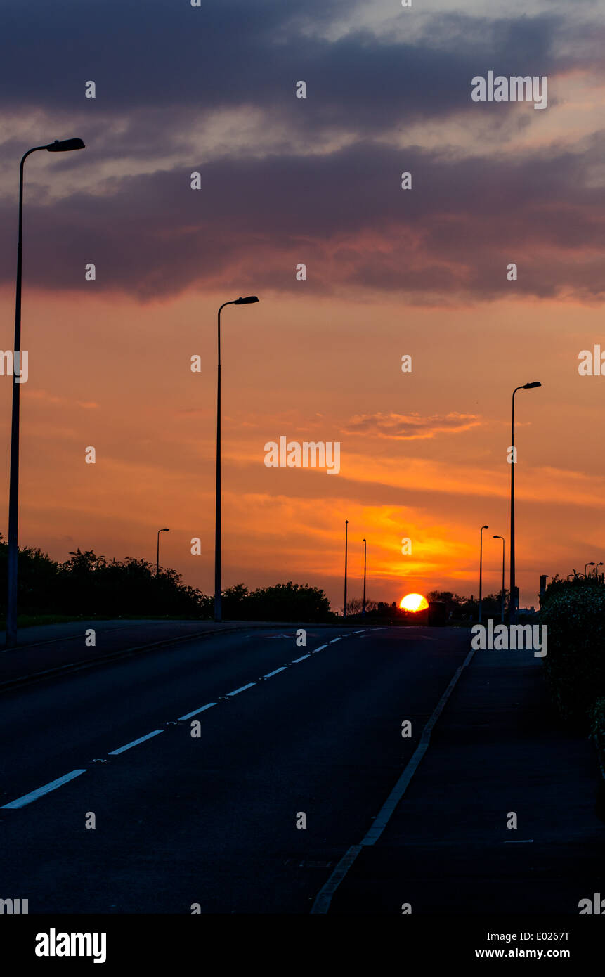 A road cast in sunset light with the sun setting. Stock Photo