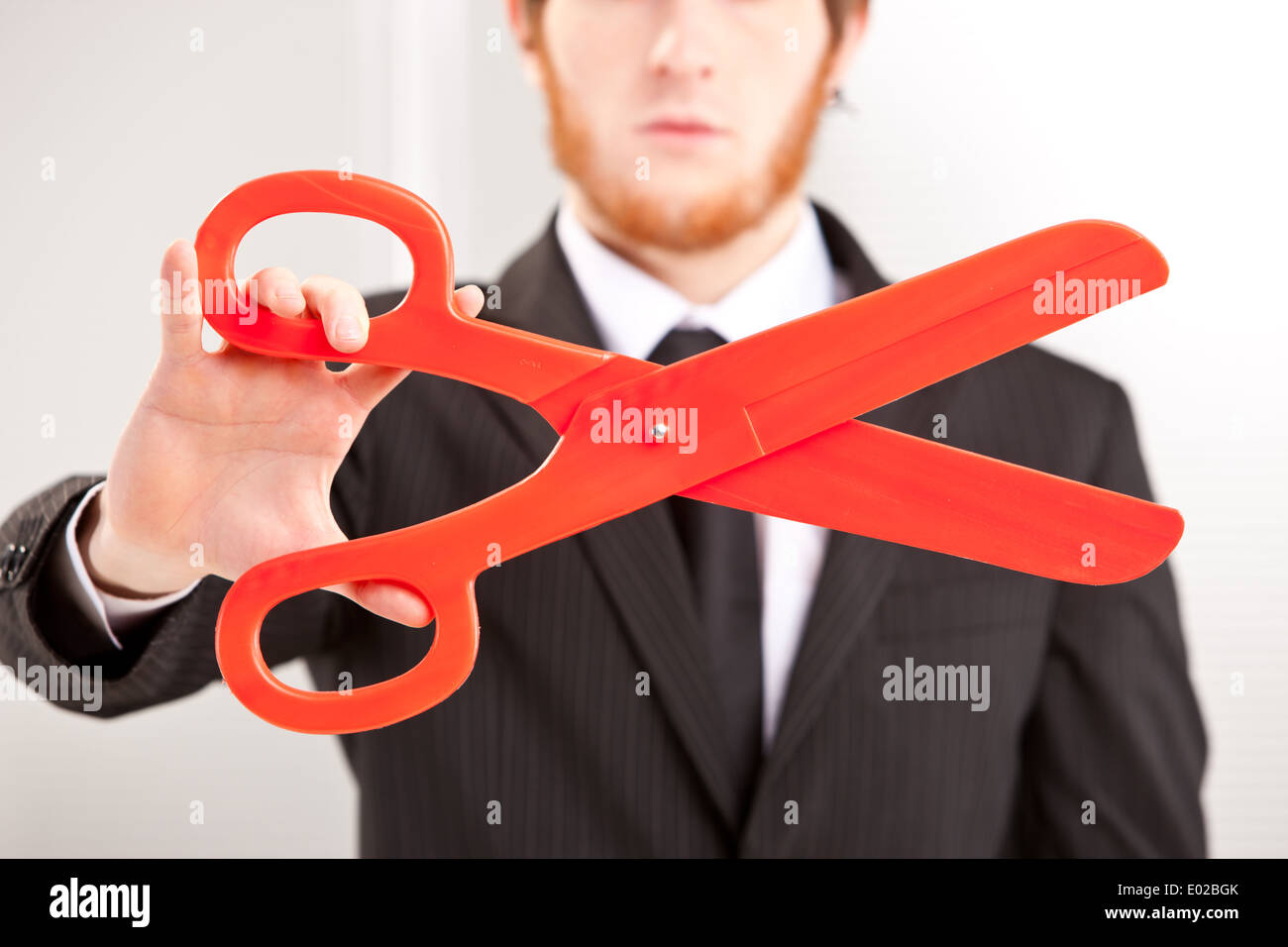 a young business man showing a big red pair of scissors Stock Photo
