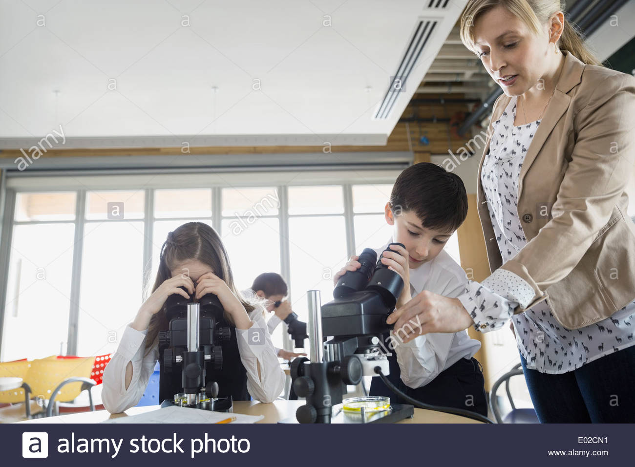 Elementary students and teacher using microscope in classroom Stock