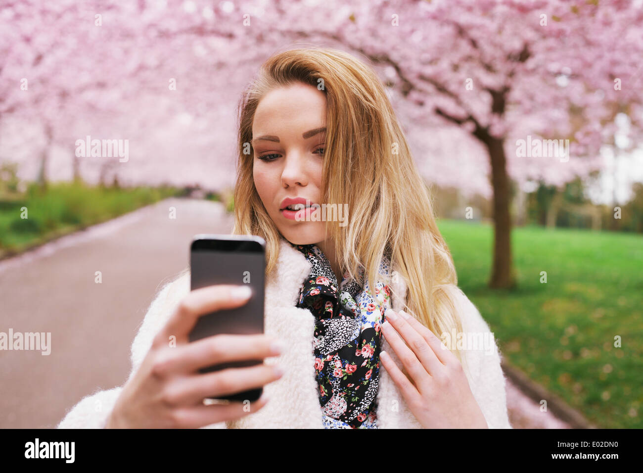 Attractive woman photographing herself at the spring garden. Beautiful young female model taking self portrait with her phone. Stock Photo