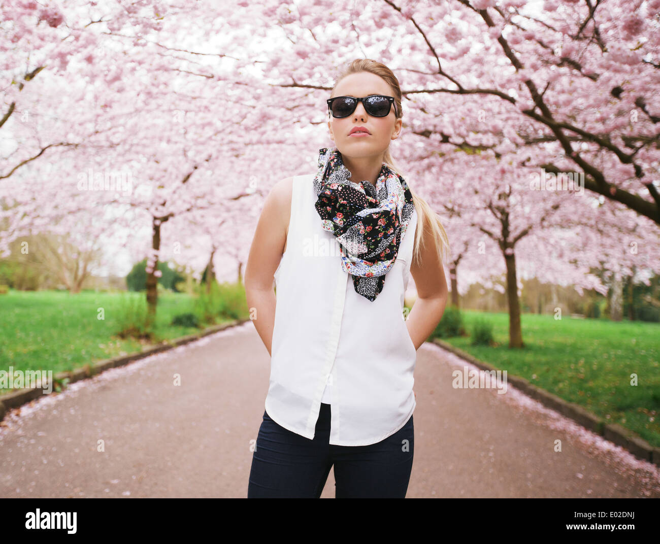 Fashionable young lady posing confidently at park. Attractive female model at spring blossom park Stock Photo