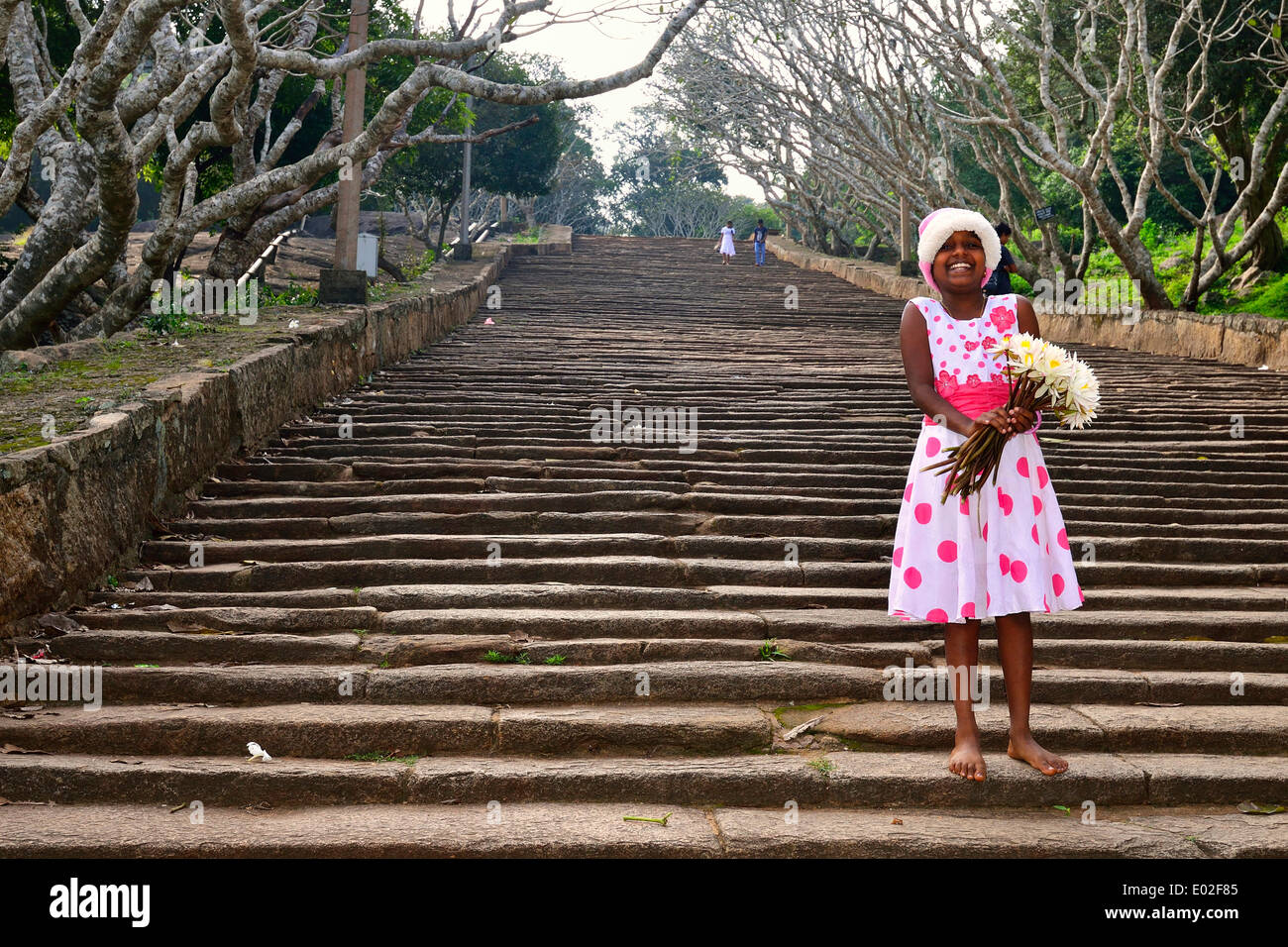 Girl with lotus flowers on the stone stairs to the Buddhist temple complex of Mihintale, Anuradhapura, North Central Province Stock Photo