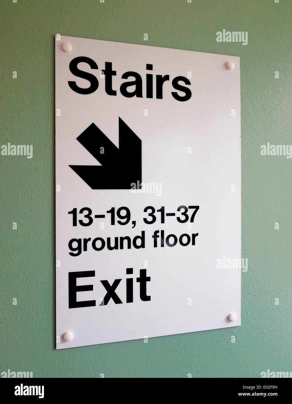 White sign attached to a wall giving directions down stairs to ground floor exit and flat