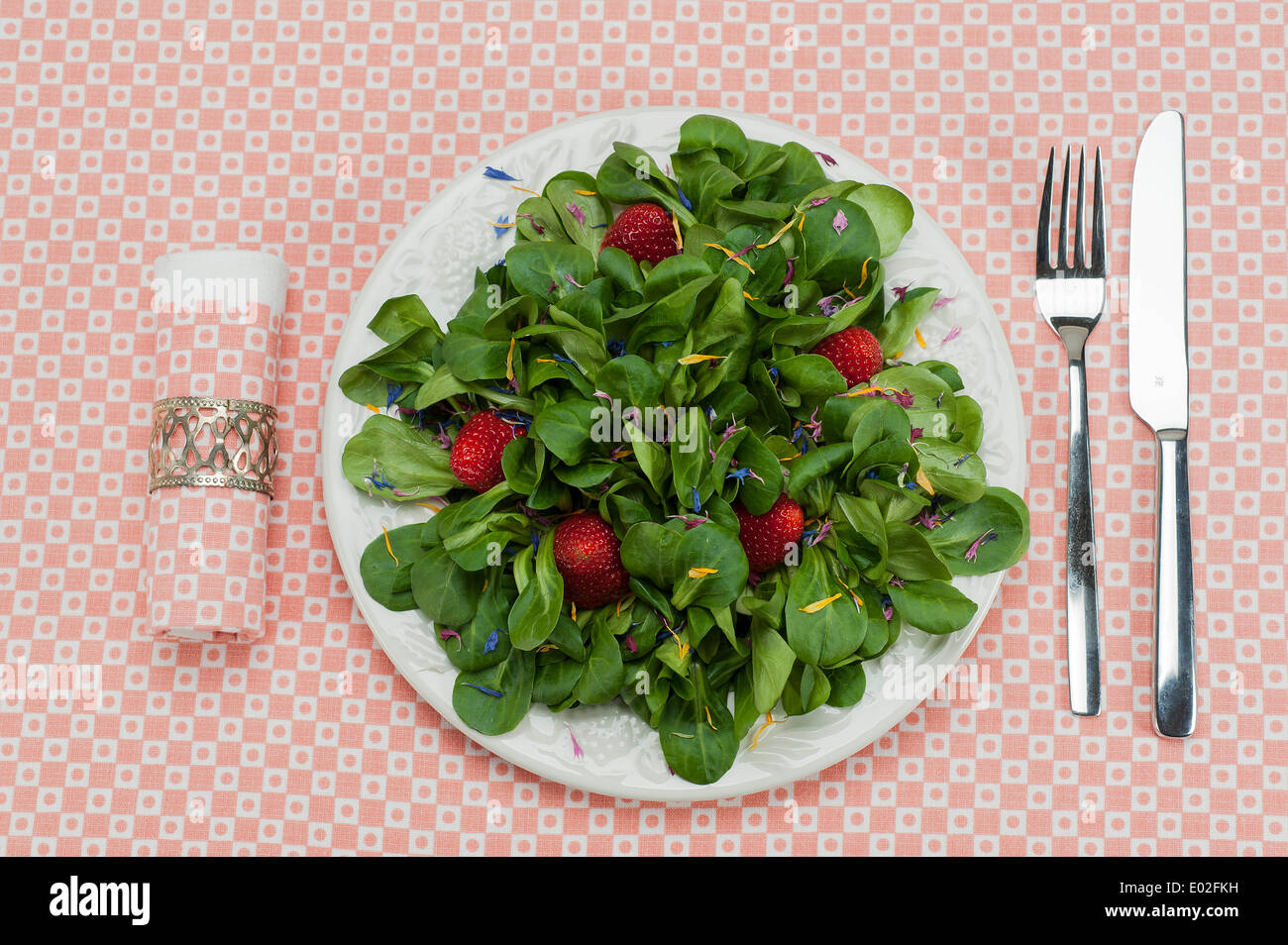 Lamb's lettuce with strawberries and flower petals served on a plate, napkin, cutlery Stock Photo