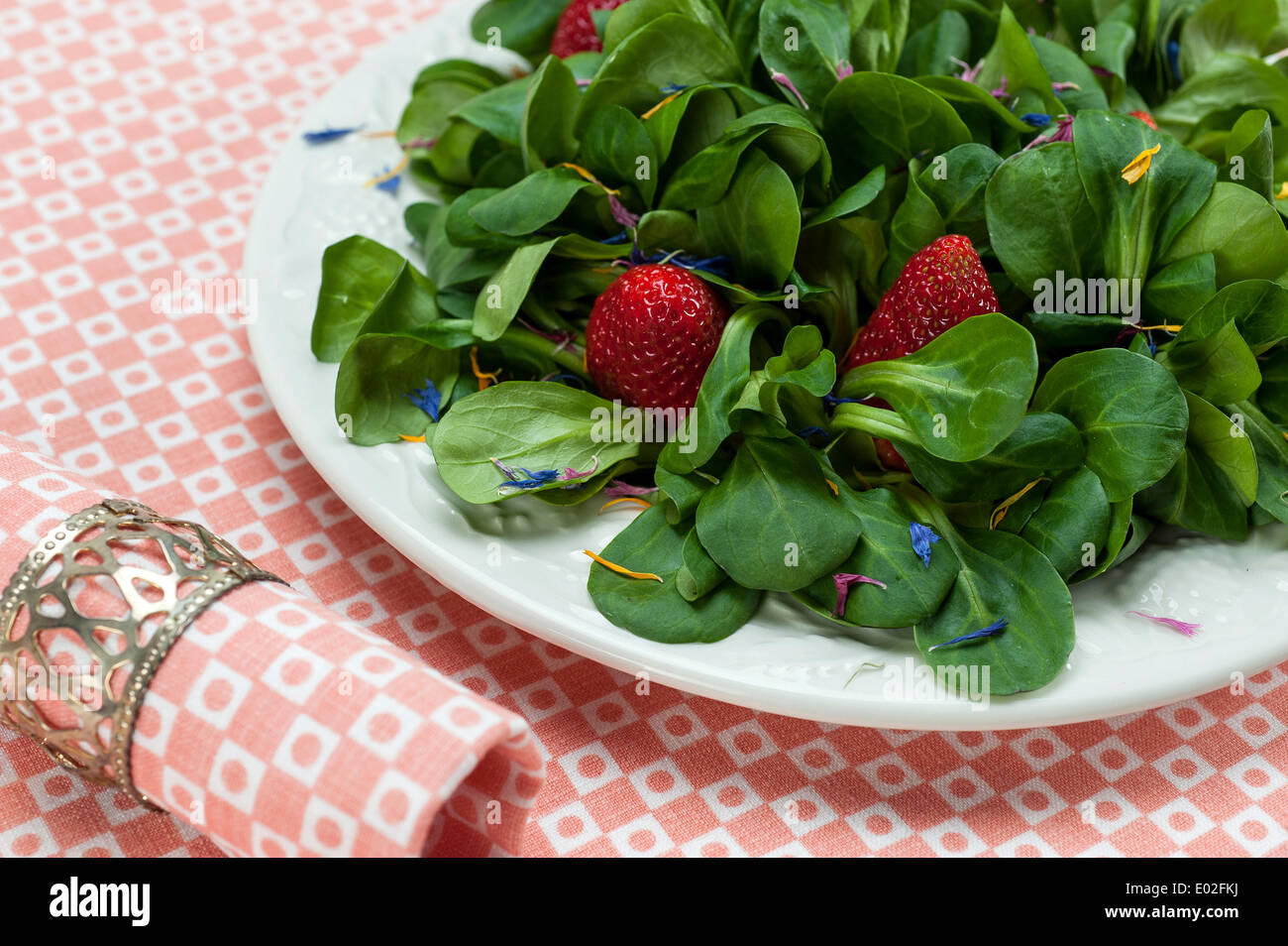 Lamb's lettuce with strawberries and flower petals served on a plate, napkin Stock Photo