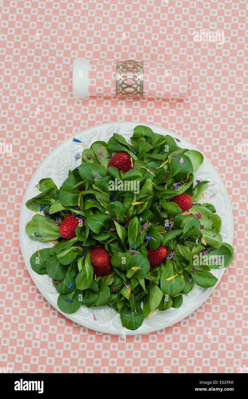 Lamb's lettuce with strawberries and flower petals served on a plate, napkin Stock Photo