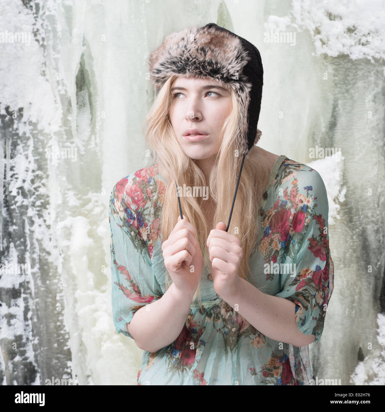 Blonde woman in front of ice covered mountain wearing summer dress and winter hat Stock Photo