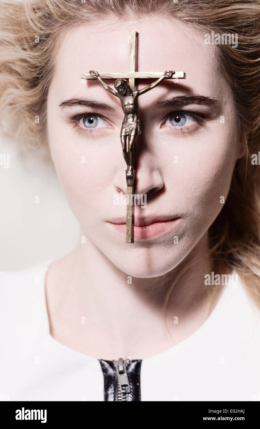 Beautiful woman with crucifix resting on her face. She is looking away with focused expression. Conceptual image of christianity, belief and hope. Stock Photo