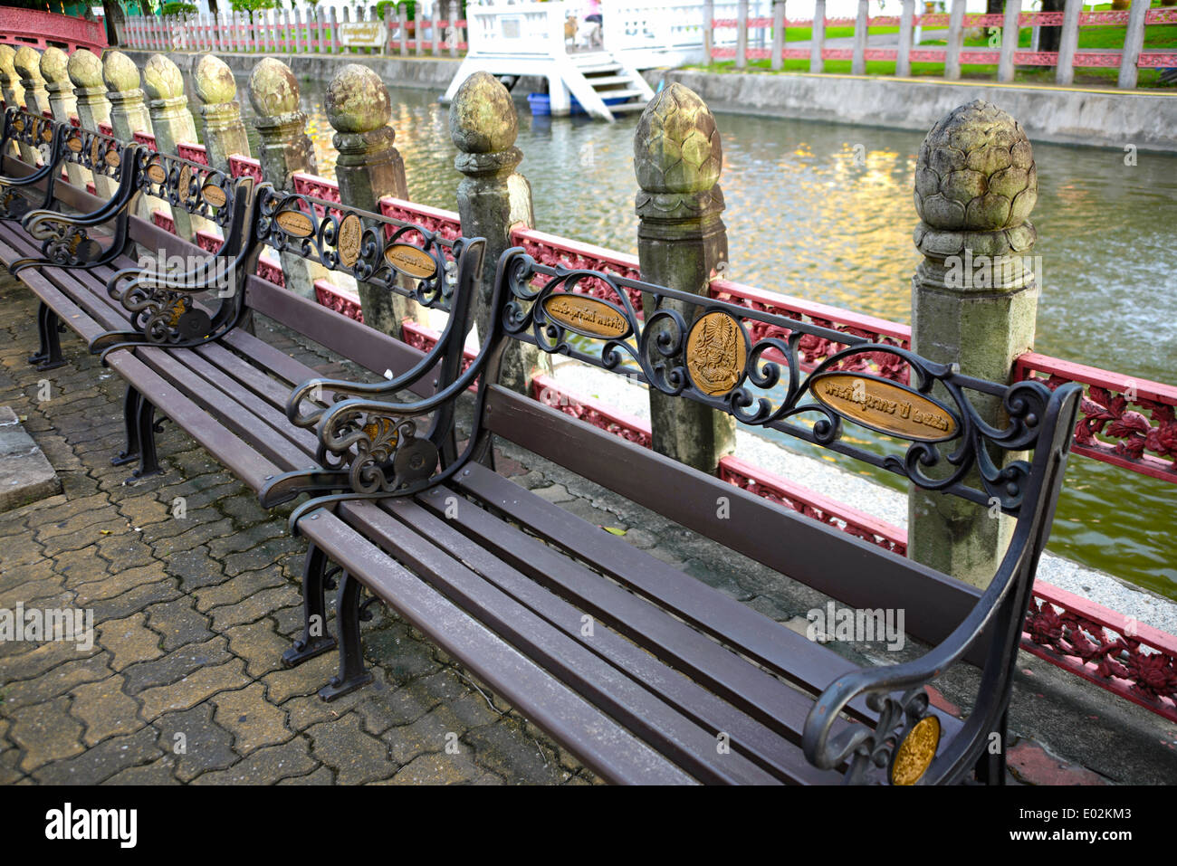 A row of metal benches in front of a small canal at a Thai temple, Bangkok, Thailand. Stock Photo