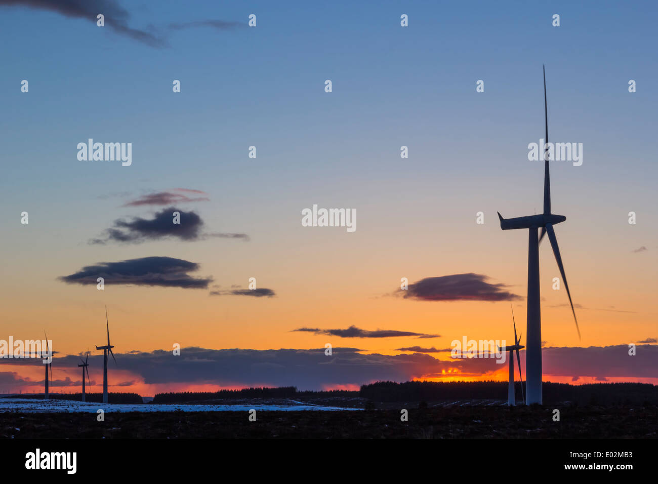 Wind Turbines silhouetted against a Fiery Orange Sunset, with Snow on the ground and some clouds in the sky. Stock Photo